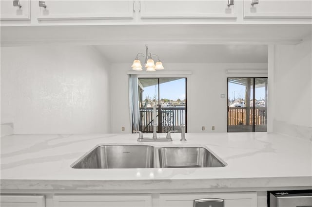 kitchen with white cabinetry, light stone countertops, a notable chandelier, and sink