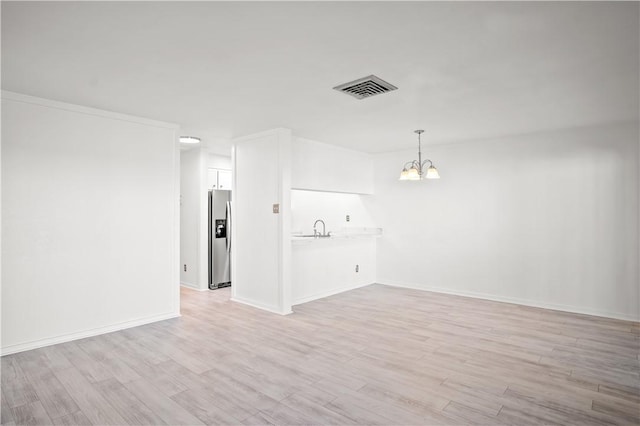 unfurnished living room with light hardwood / wood-style floors, a chandelier, and sink