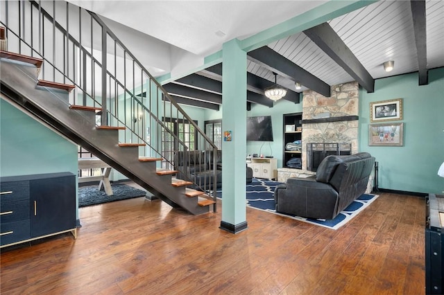 stairs with hardwood / wood-style floors, baseboards, beamed ceiling, and a stone fireplace
