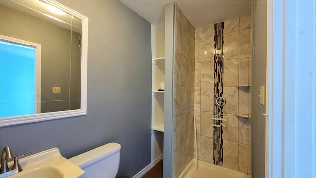 bathroom with a tile shower, toilet, and sink