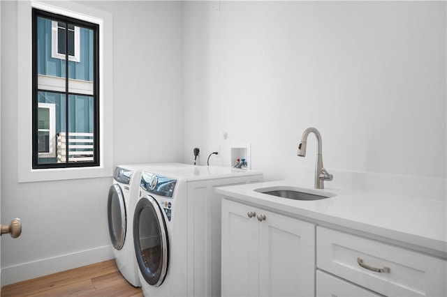 washroom featuring light wood finished floors, cabinet space, a sink, washer and dryer, and baseboards