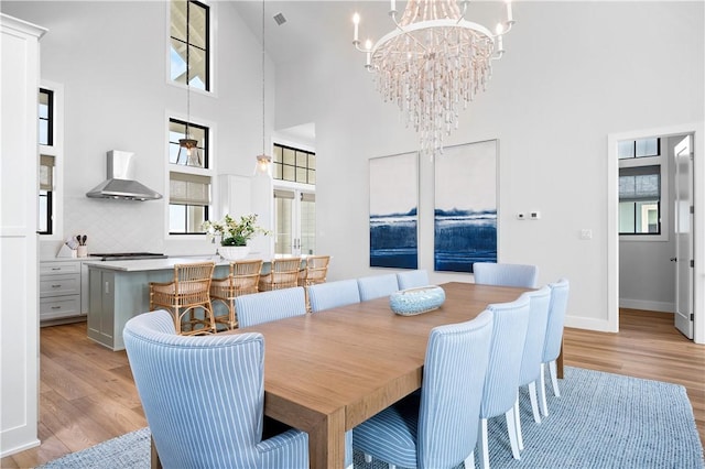 dining space featuring light wood-style flooring, a high ceiling, baseboards, and a chandelier