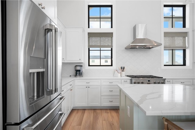 kitchen with light wood finished floors, a wealth of natural light, wall chimney range hood, range, and stainless steel fridge with ice dispenser