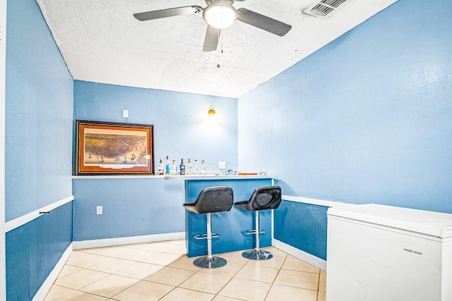 bar with ceiling fan, a textured ceiling, refrigerator, and light tile patterned flooring