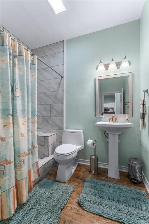 bathroom with toilet, baseboards, a tile shower, and wood finished floors