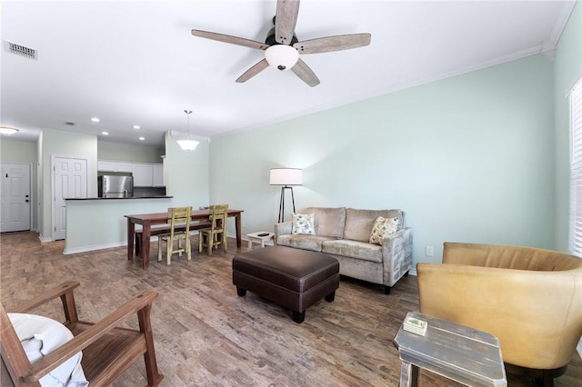 living area with crown molding, visible vents, light wood-style floors, ceiling fan, and baseboards