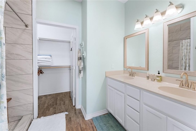 full bath with double vanity, wood finished floors, a sink, and a walk in closet