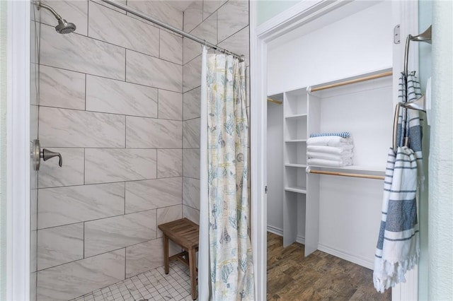 bathroom featuring a spacious closet, tiled shower, and wood finished floors