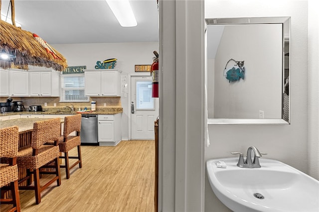 kitchen with light stone counters, white cabinetry, light wood-type flooring, sink, and stainless steel dishwasher