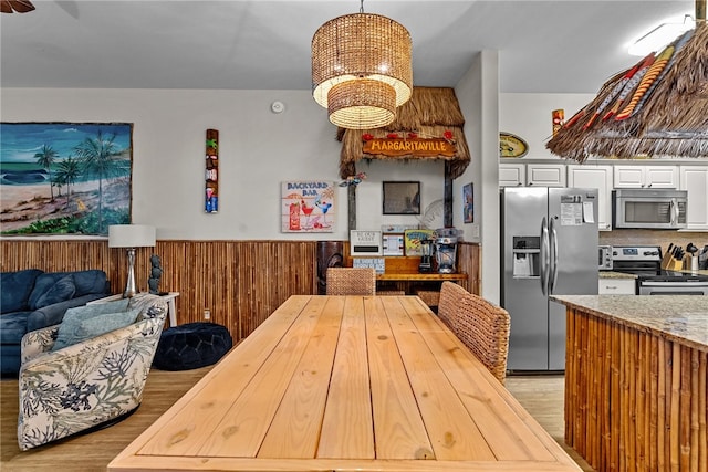 kitchen with stainless steel appliances, light hardwood / wood-style floors, white cabinetry, decorative light fixtures, and wooden walls