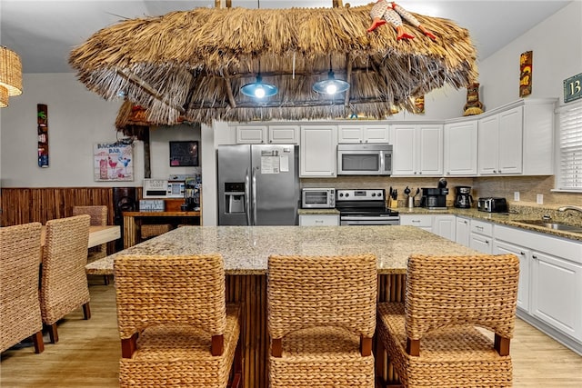 kitchen with stainless steel appliances, sink, a center island, white cabinets, and light wood-type flooring