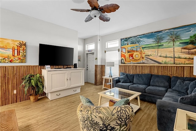 living room with light wood-type flooring, wooden walls, and ceiling fan