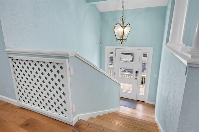 foyer entrance with baseboards, stairway, wood finished floors, and an inviting chandelier