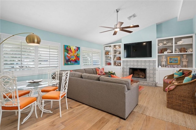 living area with a fireplace, visible vents, ceiling fan, vaulted ceiling, and wood finished floors