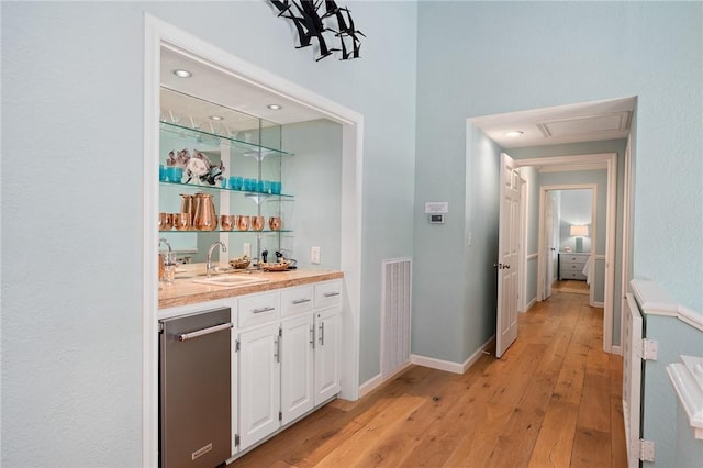 bar featuring indoor wet bar, visible vents, light wood-style flooring, a sink, and baseboards