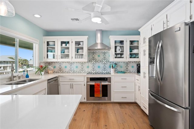 kitchen featuring stainless steel appliances, a sink, visible vents, backsplash, and wall chimney exhaust hood