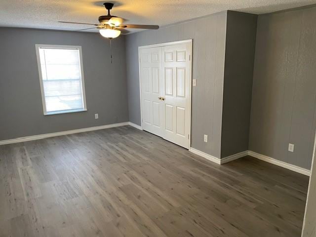 unfurnished bedroom with a textured ceiling, a closet, wood finished floors, and baseboards