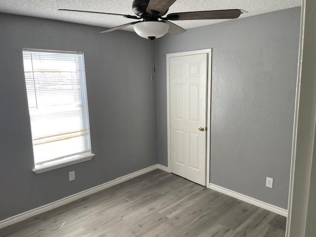 empty room featuring a wealth of natural light, a textured ceiling, baseboards, and wood finished floors