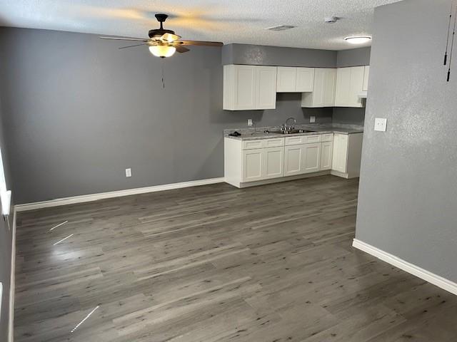 kitchen featuring dark wood-style floors, baseboards, white cabinetry, and a sink