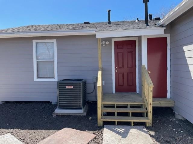 doorway to property featuring a shingled roof and central AC unit