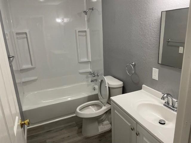 bathroom with a textured wall, toilet, wood finished floors, vanity, and  shower combination