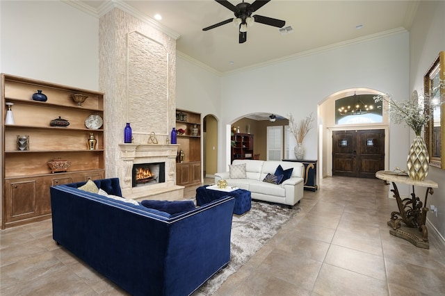 living room featuring a stone fireplace, ornamental molding, ceiling fan, and a high ceiling