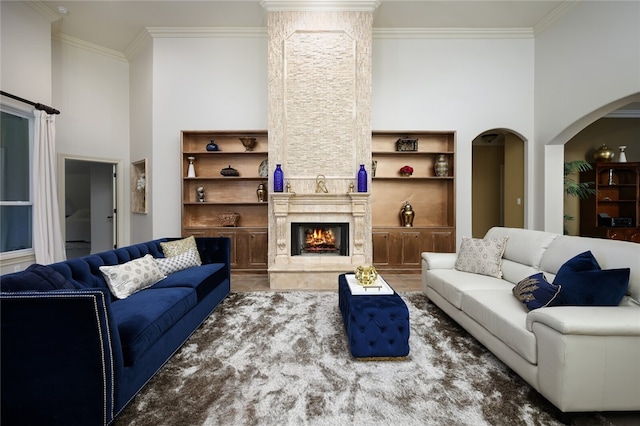 living room featuring a high ceiling, a premium fireplace, ornamental molding, and built in shelves