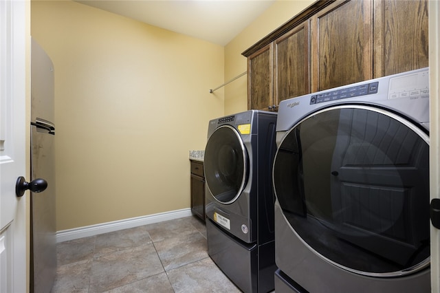 clothes washing area with light tile patterned floors, washer and clothes dryer, and cabinets