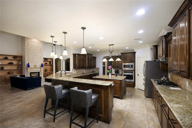 kitchen with stainless steel appliances, a kitchen breakfast bar, an island with sink, and hanging light fixtures