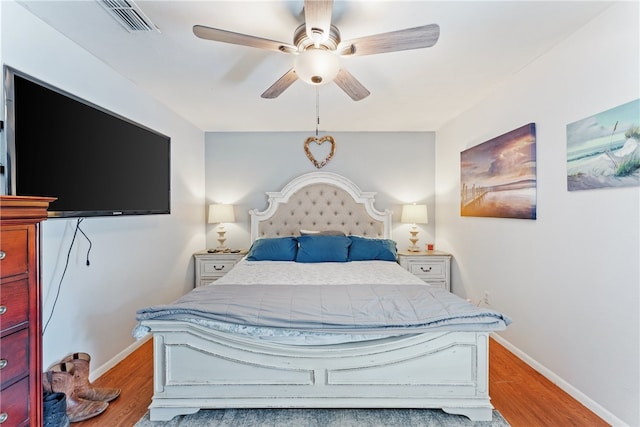 bedroom with a ceiling fan, visible vents, baseboards, and wood finished floors