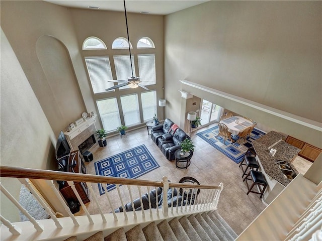 living area featuring tile patterned floors, a tiled fireplace, a ceiling fan, a towering ceiling, and stairway