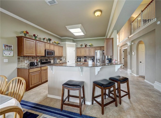 kitchen featuring backsplash, a kitchen bar, visible vents, appliances with stainless steel finishes, and dark stone countertops