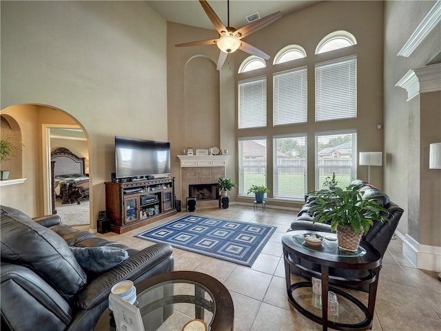 tiled living room featuring visible vents, a towering ceiling, a fireplace, baseboards, and a ceiling fan