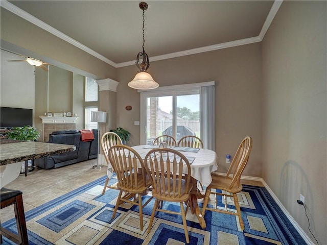 dining space featuring a tiled fireplace, ornamental molding, baseboards, and ceiling fan