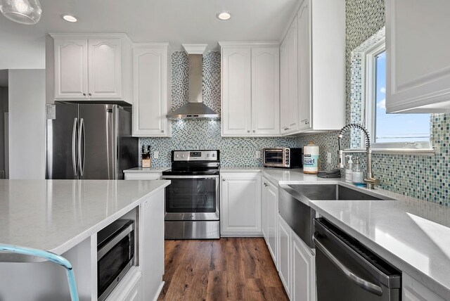 kitchen featuring appliances with stainless steel finishes, white cabinetry, wall chimney range hood, and decorative backsplash