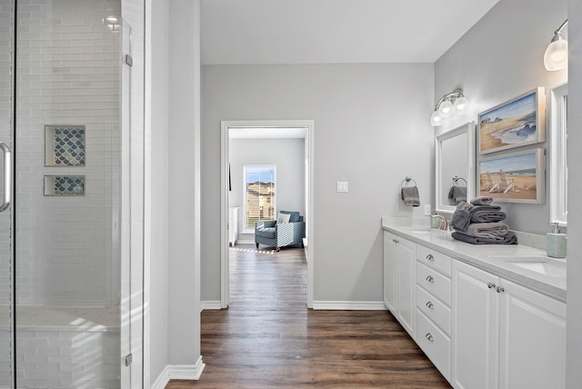 full bath with double vanity, a sink, a shower stall, wood finished floors, and baseboards