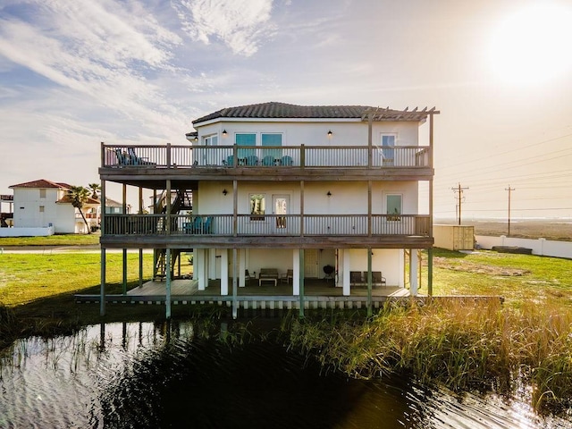 back of house featuring a patio area, a yard, a deck with water view, and stucco siding