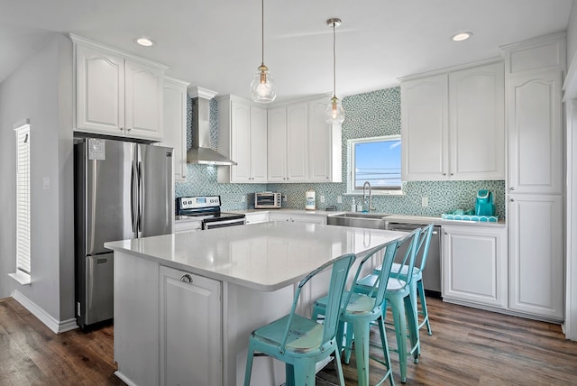 kitchen featuring a center island, appliances with stainless steel finishes, white cabinetry, a sink, and wall chimney range hood