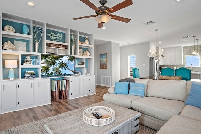 living room with ceiling fan with notable chandelier, visible vents, recessed lighting, and wood finished floors