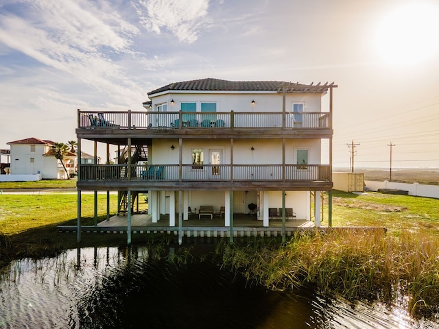 rear view of property featuring a balcony, a yard, and a deck with water view