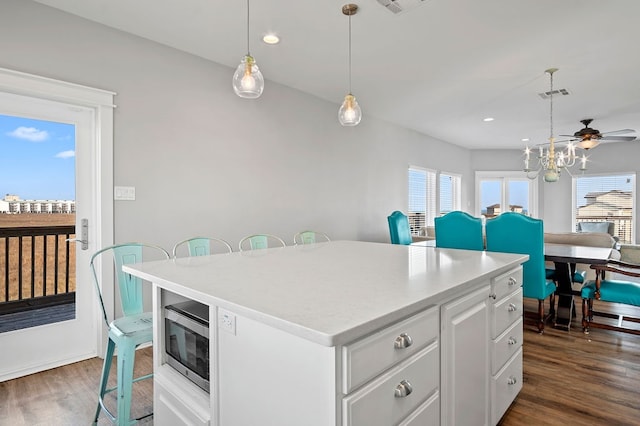 kitchen featuring plenty of natural light, a kitchen island, stainless steel microwave, and dark wood-style flooring