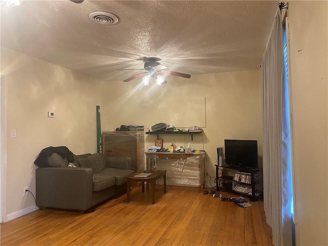 sitting room with wood-type flooring, a ceiling fan, a textured ceiling, and visible vents
