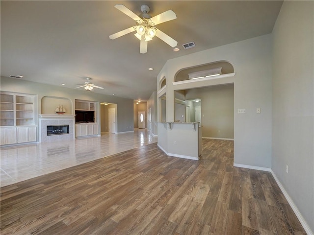 unfurnished living room featuring a tiled fireplace, dark hardwood / wood-style flooring, lofted ceiling, and ceiling fan