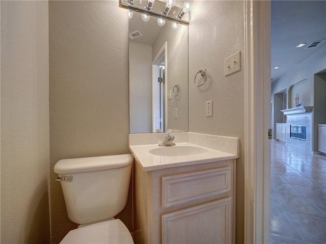 bathroom featuring vanity, toilet, a tiled fireplace, and tile patterned flooring