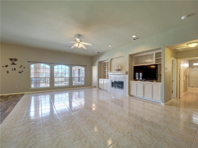 unfurnished living room featuring a tiled fireplace, light tile patterned floors, built in shelves, and ceiling fan