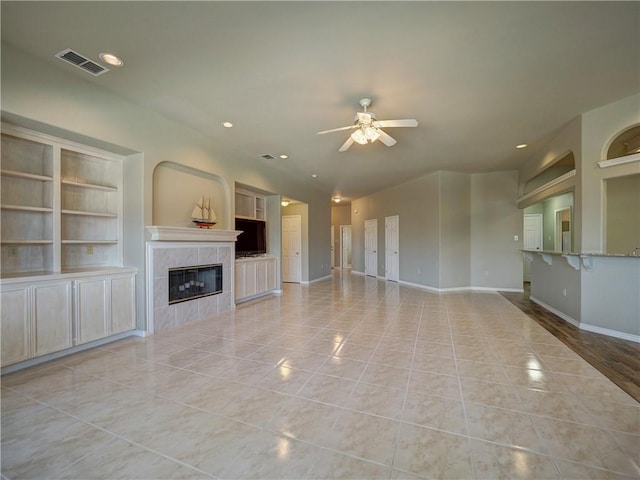 unfurnished living room with a tiled fireplace, light tile patterned flooring, ceiling fan, and built in shelves