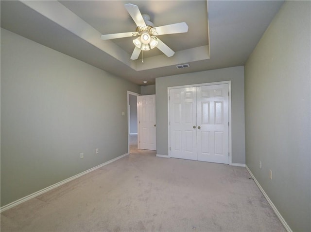 unfurnished bedroom featuring a closet, light carpet, ceiling fan, and a tray ceiling