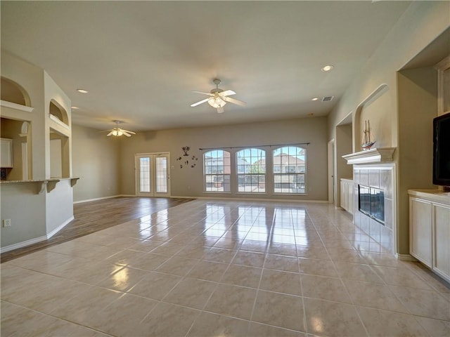 unfurnished living room featuring a tiled fireplace, light tile patterned flooring, built in features, and ceiling fan