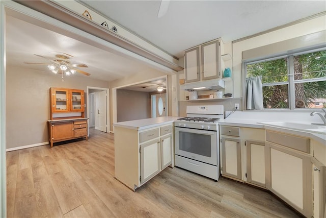 kitchen with kitchen peninsula, white gas range, light hardwood / wood-style floors, cream cabinetry, and sink