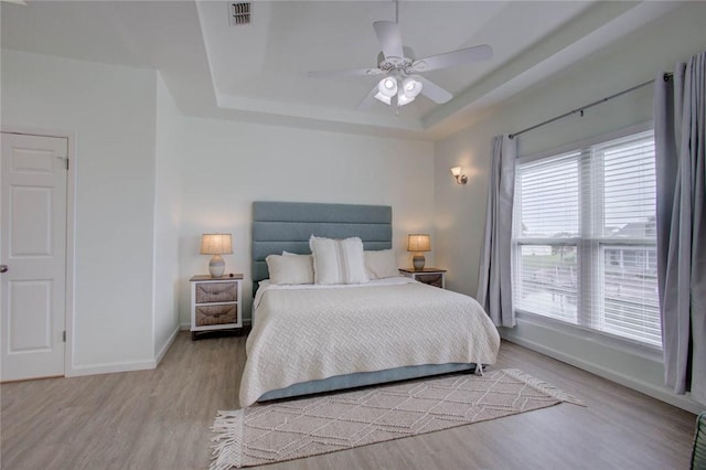 bedroom featuring a tray ceiling, multiple windows, ceiling fan, and light hardwood / wood-style floors